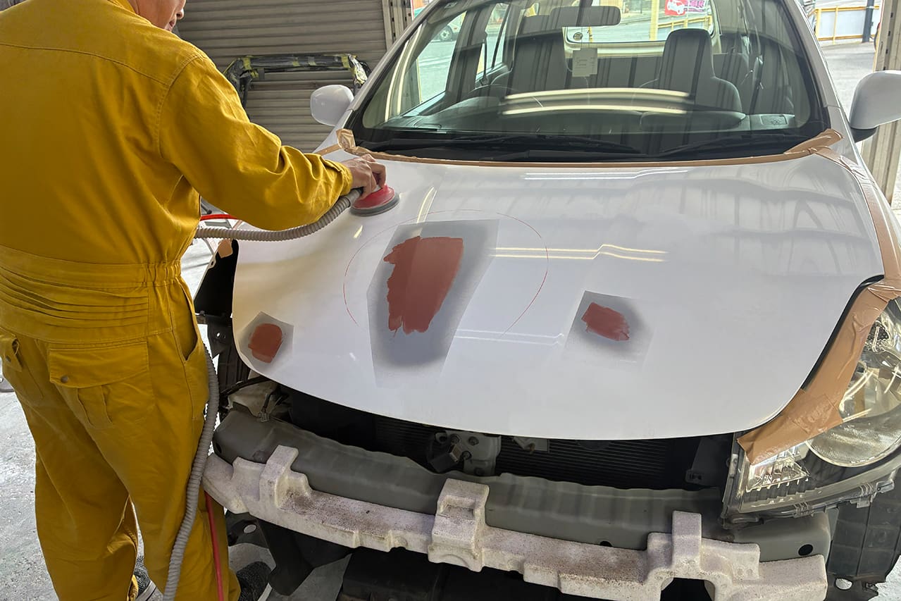 車のボンネットを研磨・修理している作業員